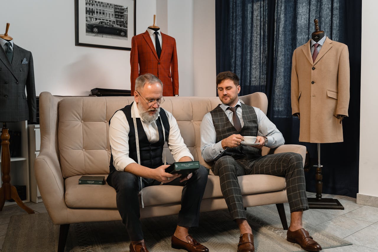 Two well-dressed men enjoying tea in an elegant tailoring workshop.